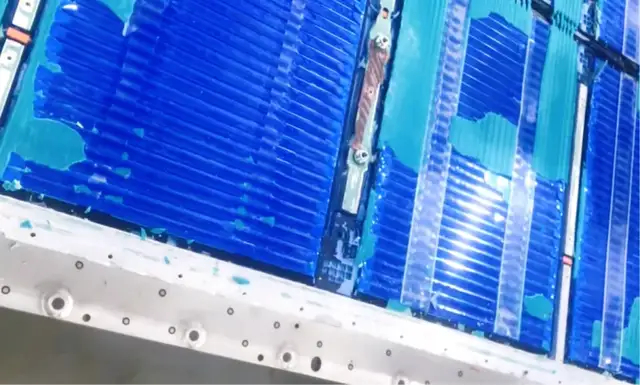 A disassembled BYD Blade battery pack showing the long, flat LFP cells stacked side by side inside the pack, with aluminium side plates and cell-to-cell busbars visible.