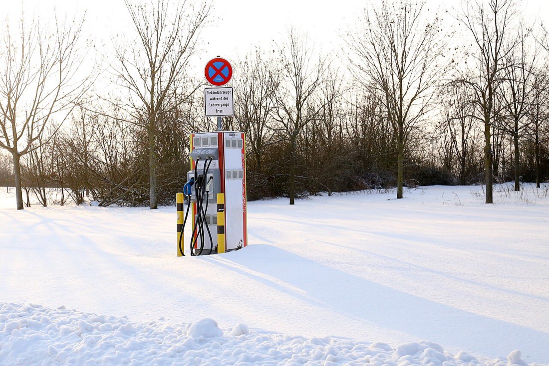 An EV charging station in winter snow — the conditions where heat-pump thermal management matters most